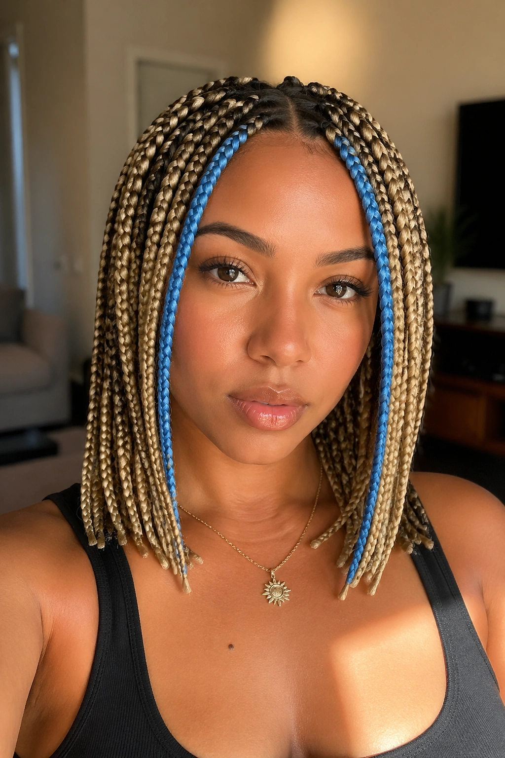 Close-up of a real woman with medium box braids and blue face-framing pieces in warm window light.