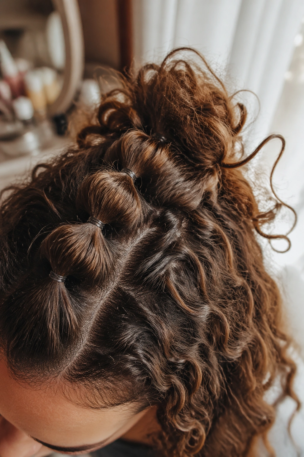 Close-up of a bubble crown bun with elastic sections in soft bedroom light.