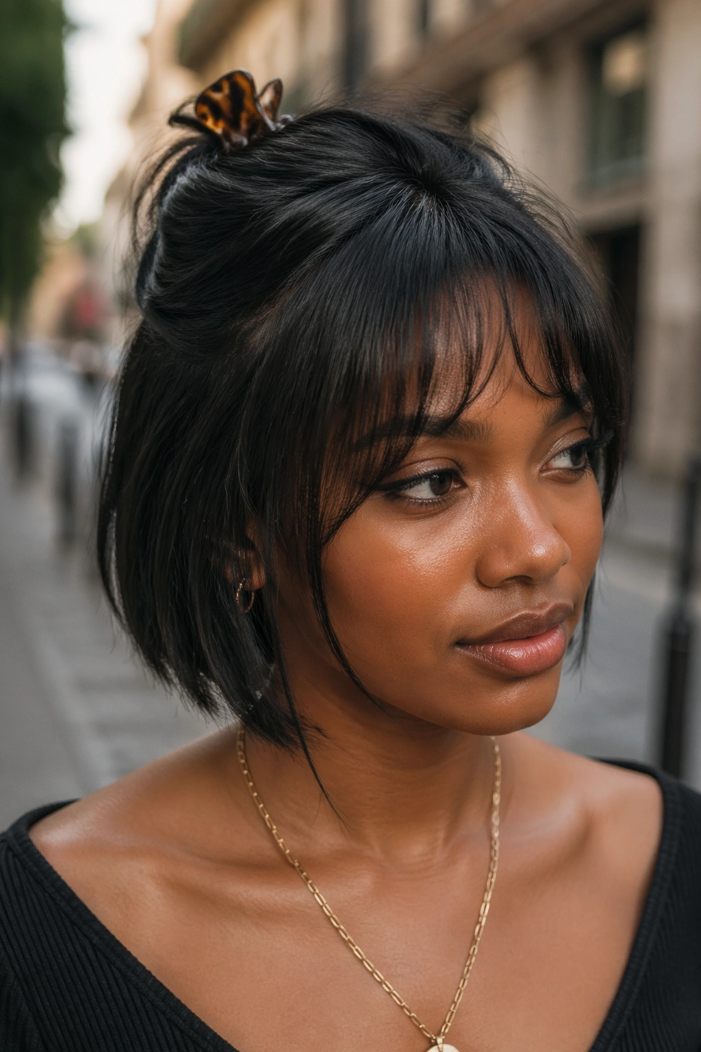 Close-up of a real Black woman wearing a claw-clip half-up with wispy bangs on a bob, soft daylight.