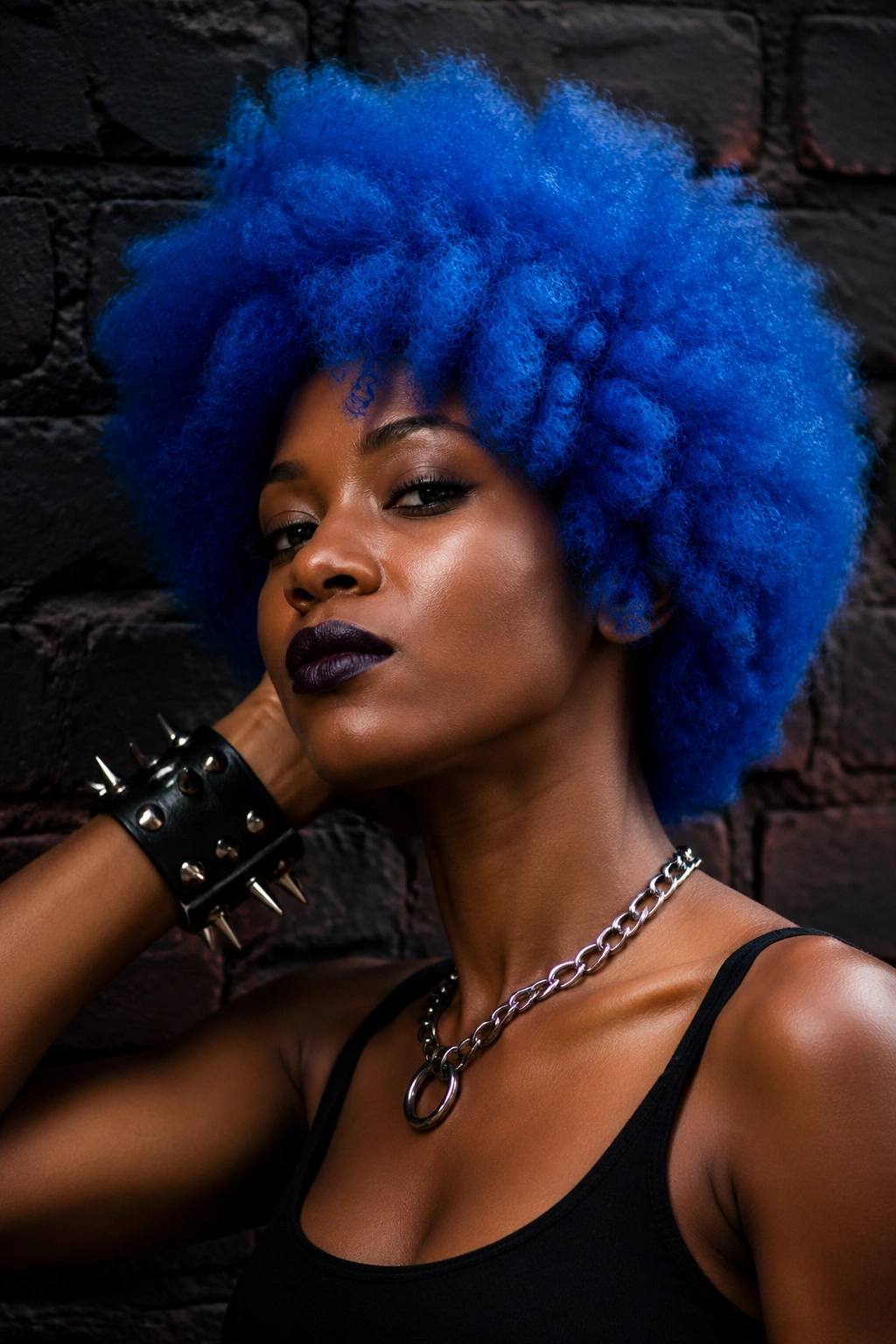 Woman with electric blue afro and punk accessories against brick wall.
