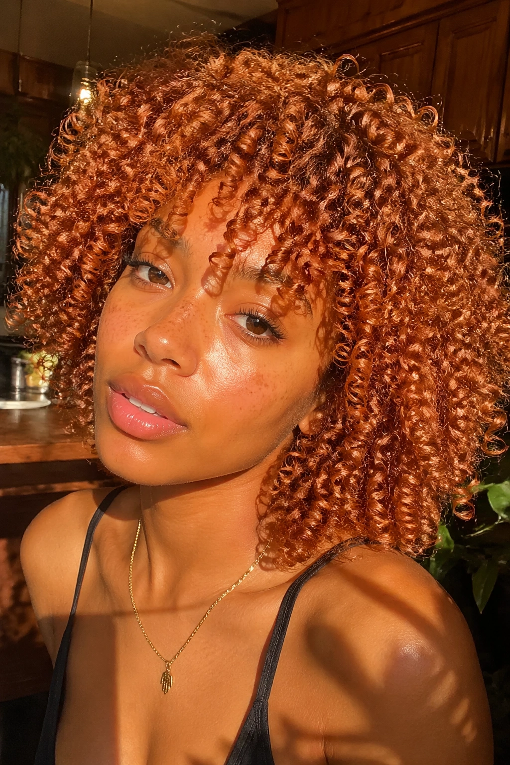 Real woman with copper-toned wash-and-go curls under warm light