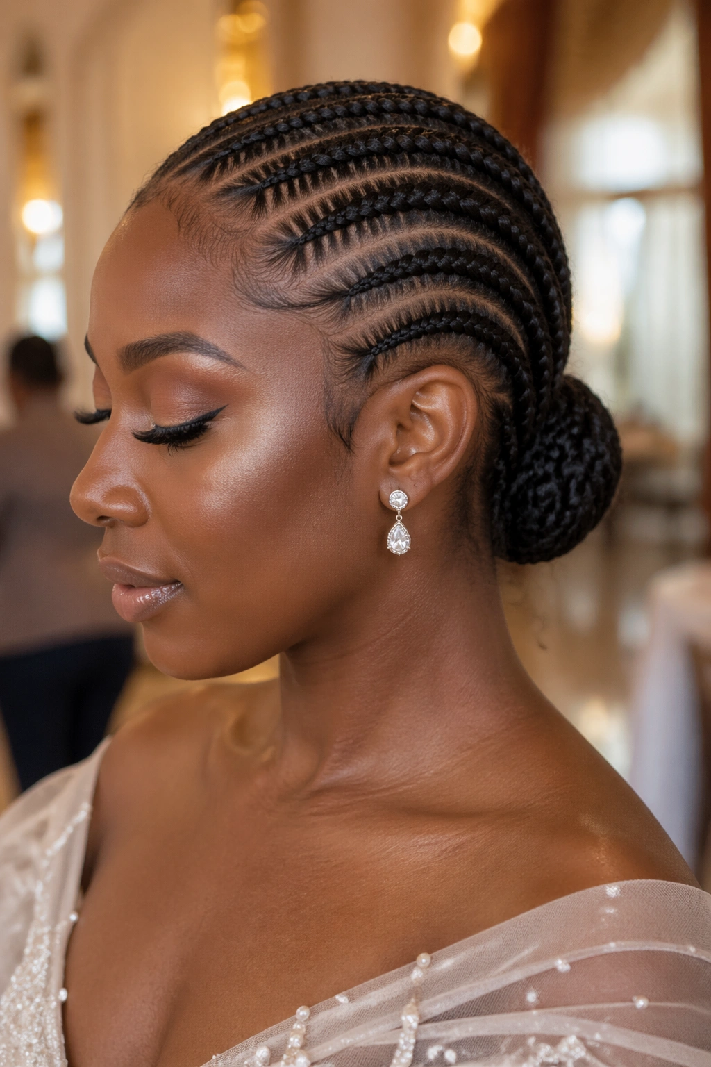 Close-up of a woman with a tucked cornrow low chignon in warm wedding venue light