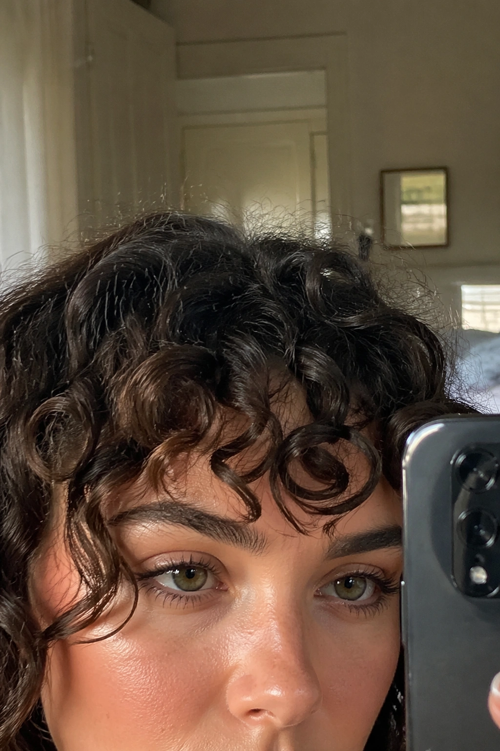 Close-up of a curly fringe on a square-face in a bedroom mirror