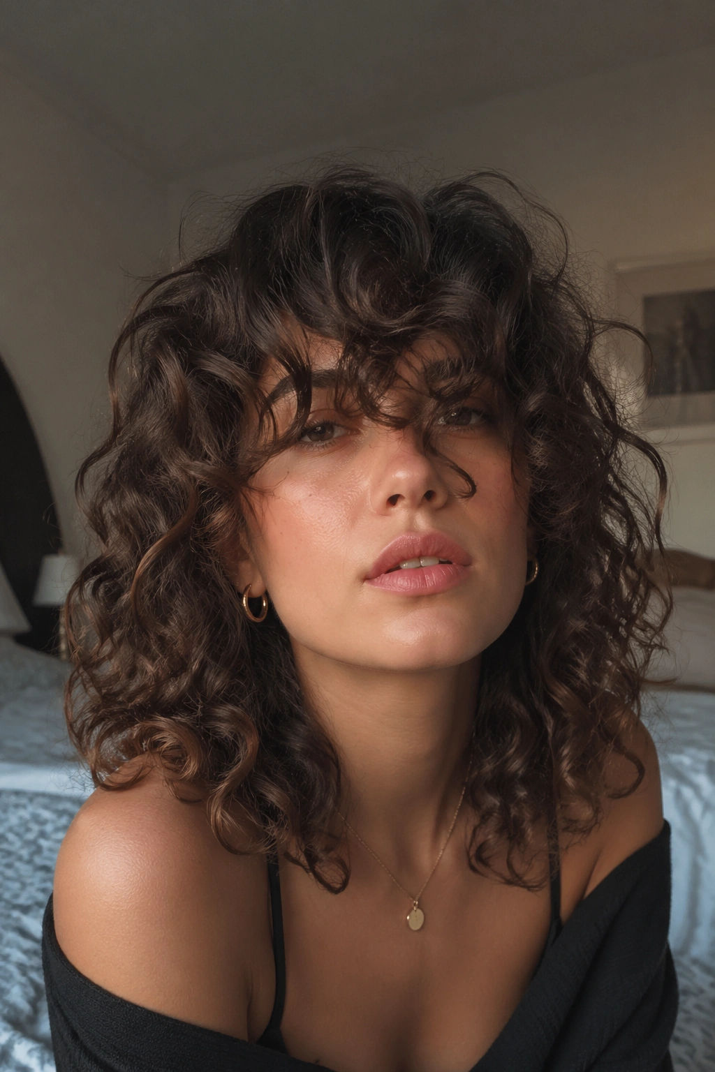 Portrait of a person with medium curly cut and long overgrown bangs by window light.