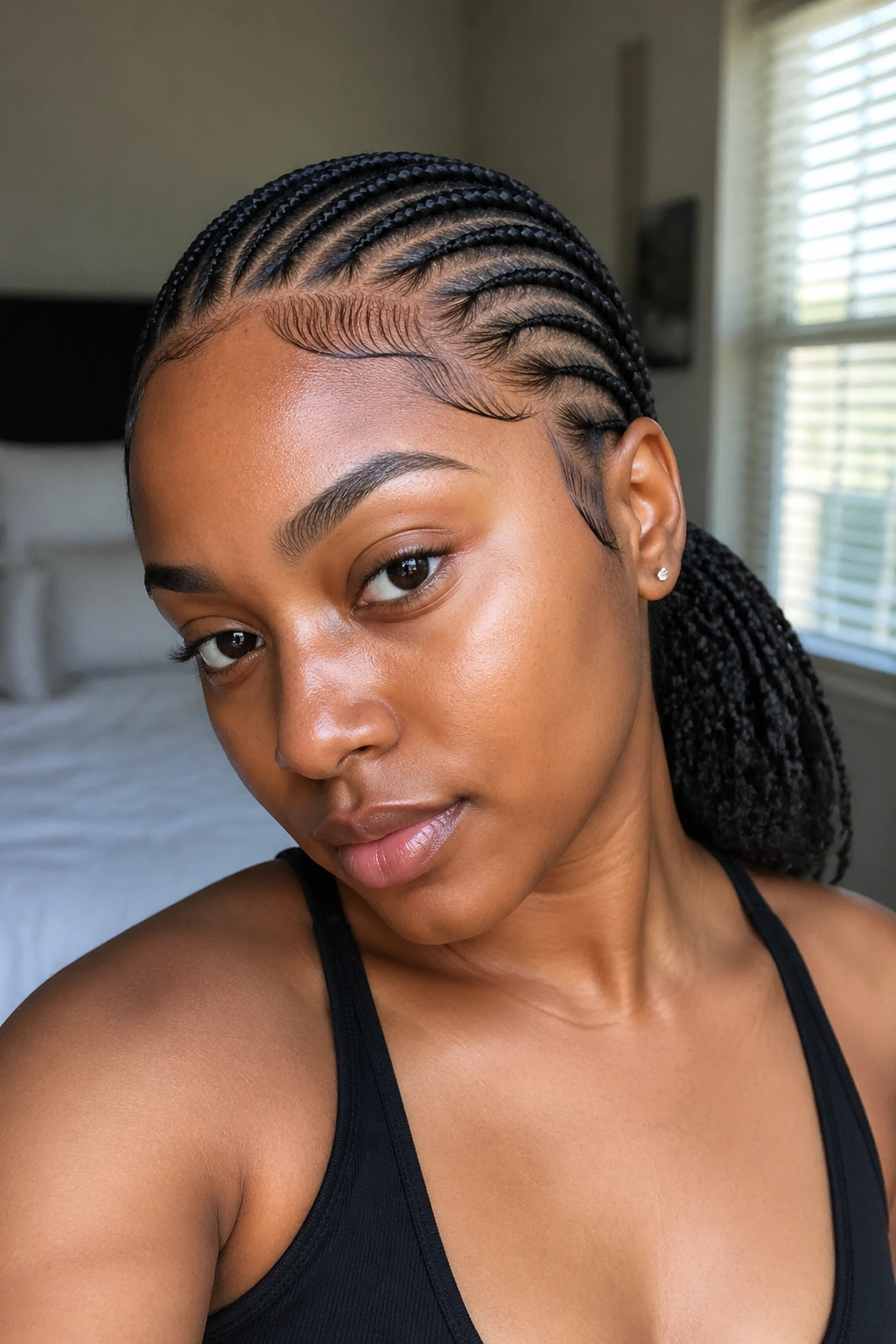 Close-up portrait of curved cornrows arcing into a mid ponytail on a real woman, soft bedroom light
