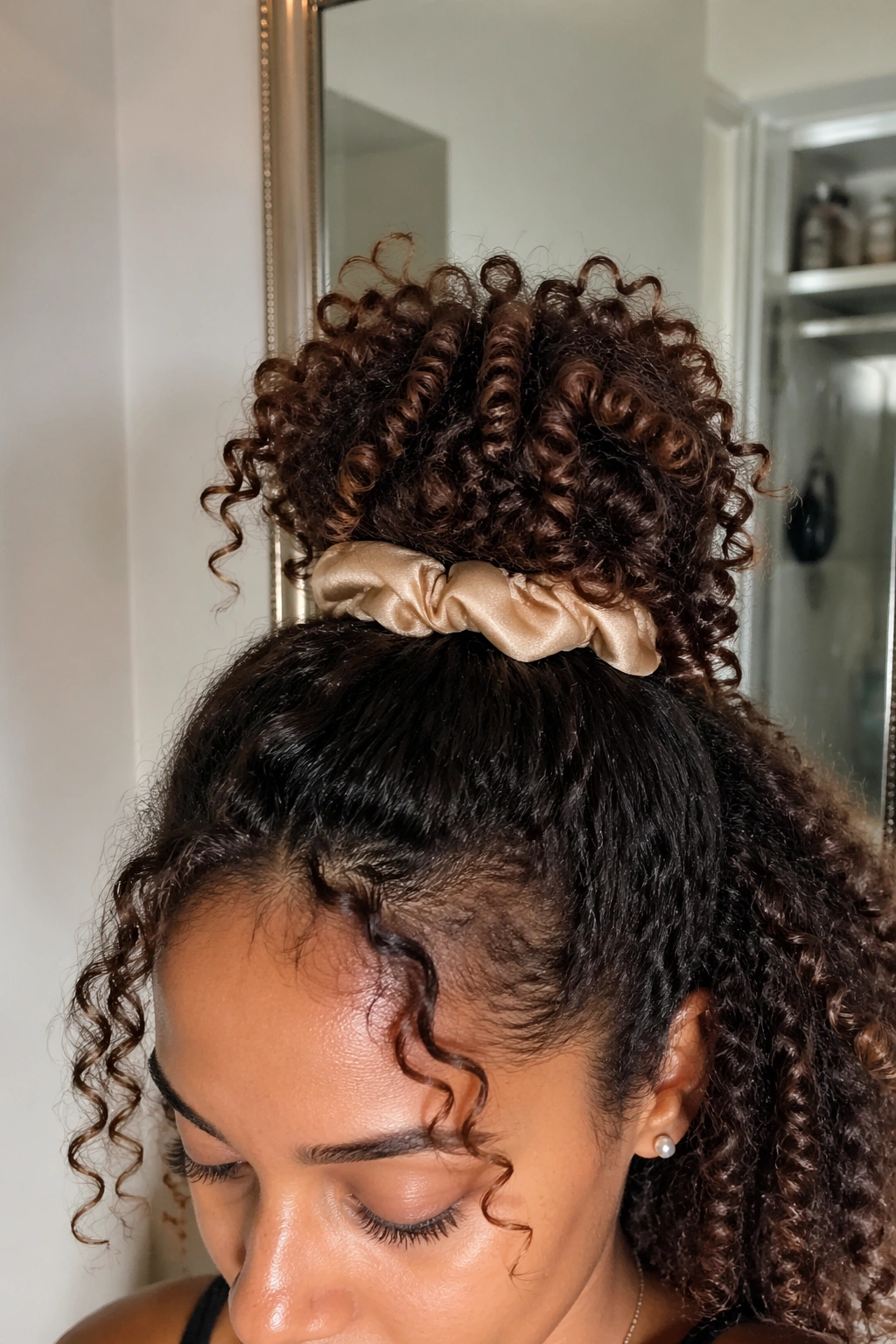 Close-up detail of half-up pineapple puff on 3b curls in a mirror-lit bathroom.