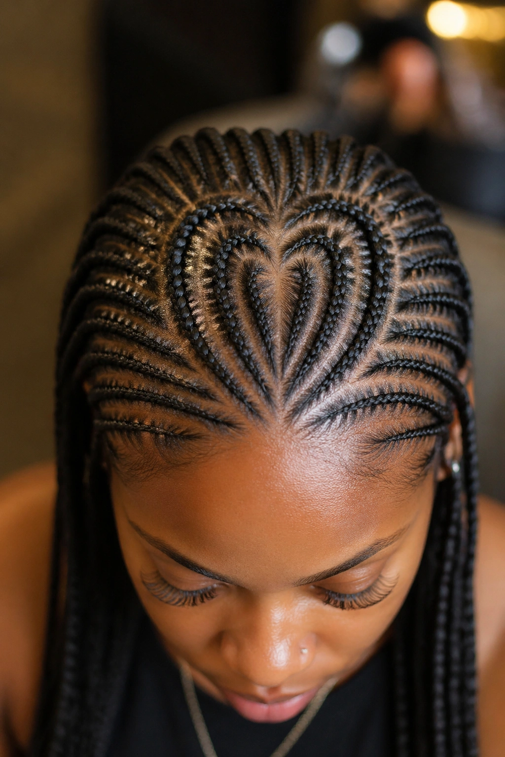 Close-up of a real woman's head showing a heart-shaped crown part with radiating small stitch cornrows.