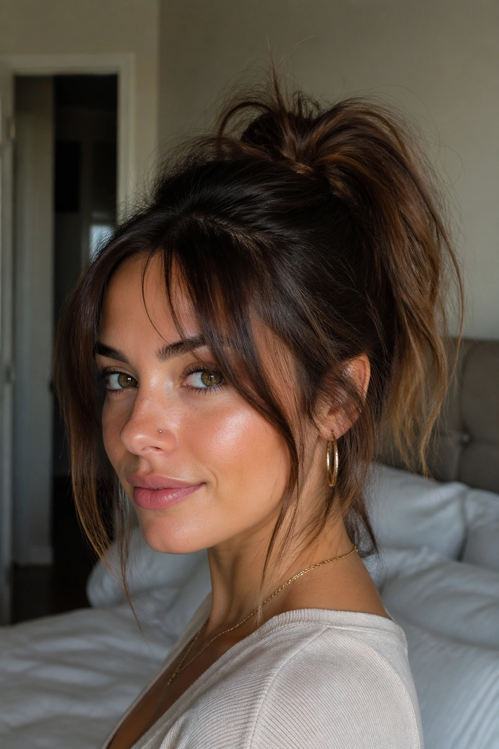 Close-up portrait of a real woman with a high messy ponytail and curtain bangs, illuminated by natural window light.