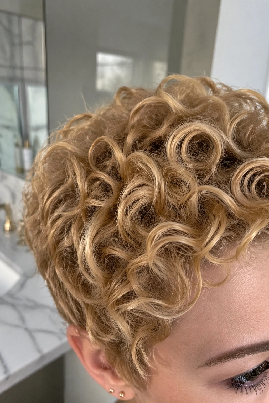 Close-up detail of honey blonde curly pixie crown in bathroom vanity.