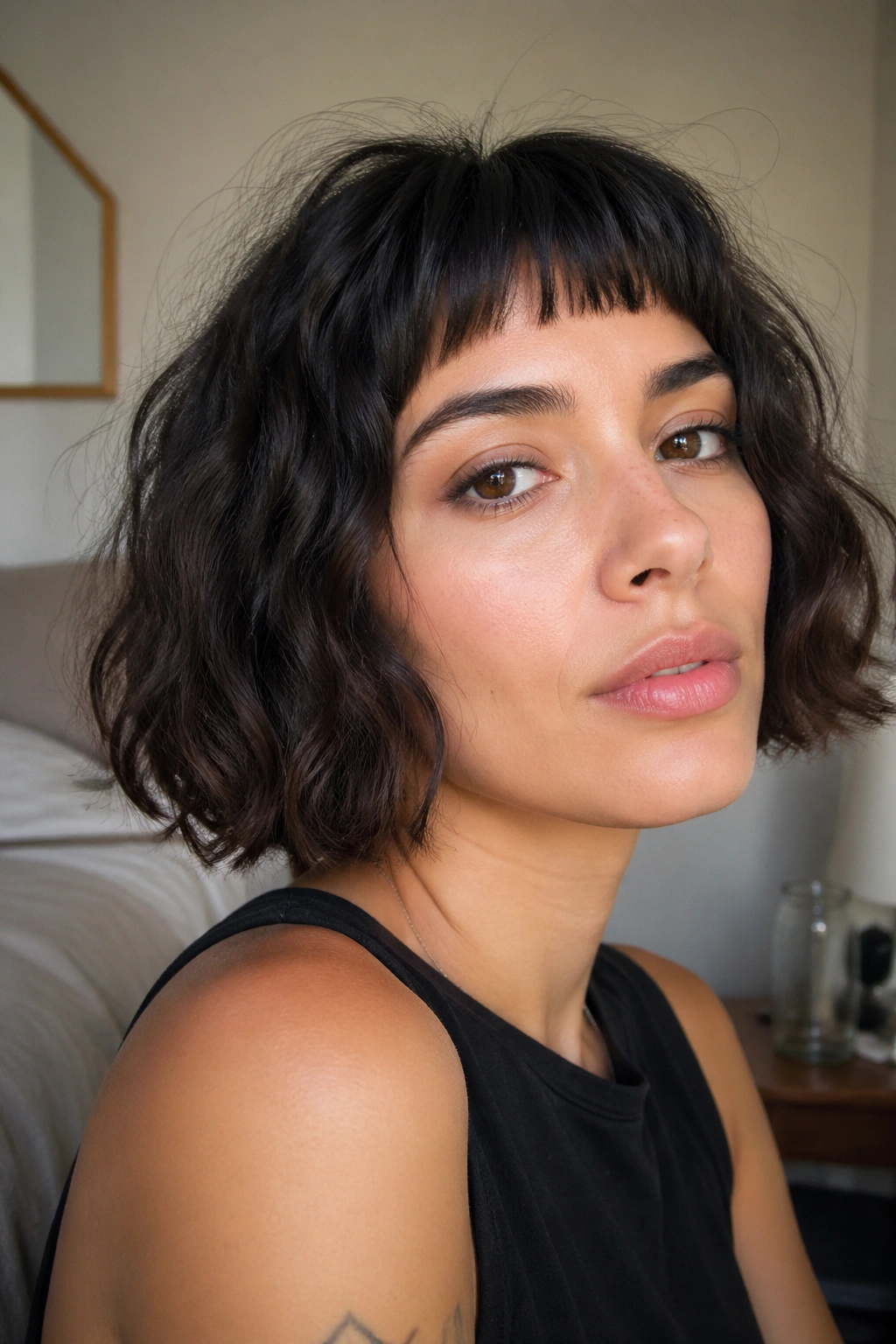 Close-up of a real woman with a micro fringe bob and thick wavy hair in window light.