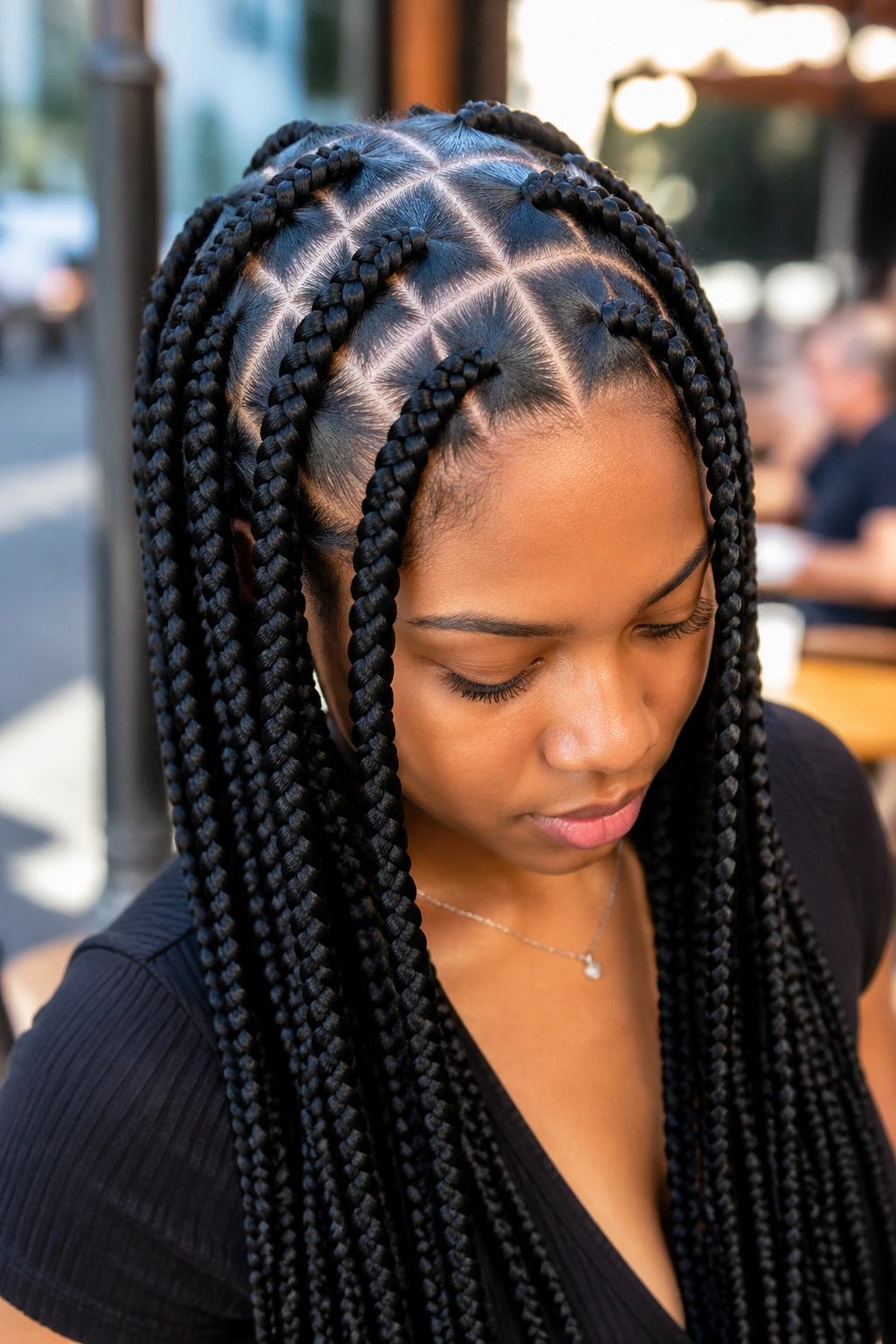 Close-up portrait of a woman with oversized-part long box braids in an outdoor cafe setting.
