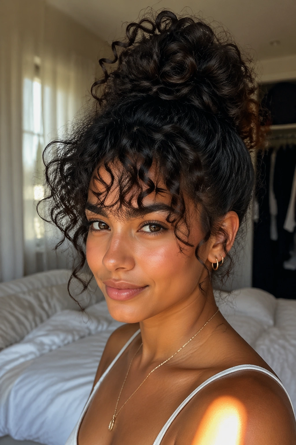 Close-up of a real woman with a high pineapple bun and curly bangs in warm window light