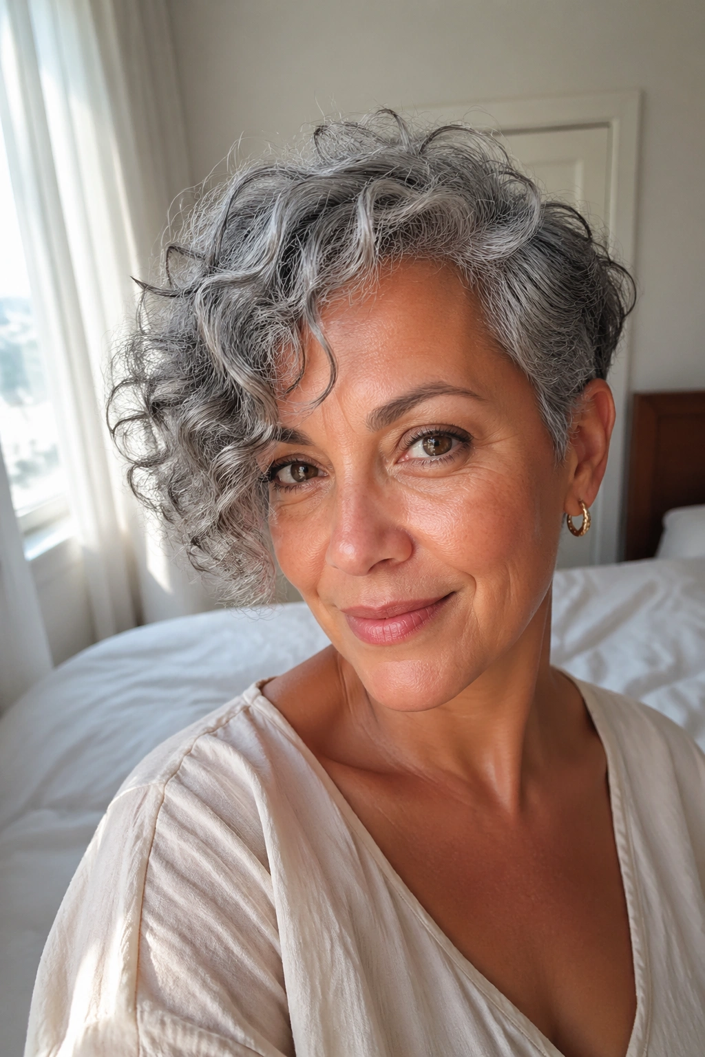 Close-up portrait of a woman with grey curly hair and a side-swept bang catching light.