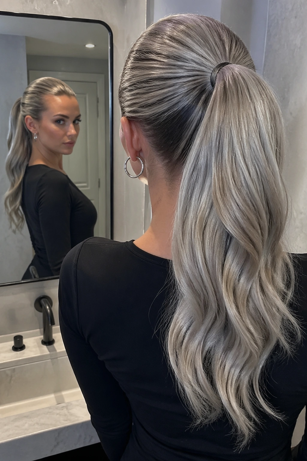 Over-the-shoulder view of silver ash weave ponytail in cool bathroom light.