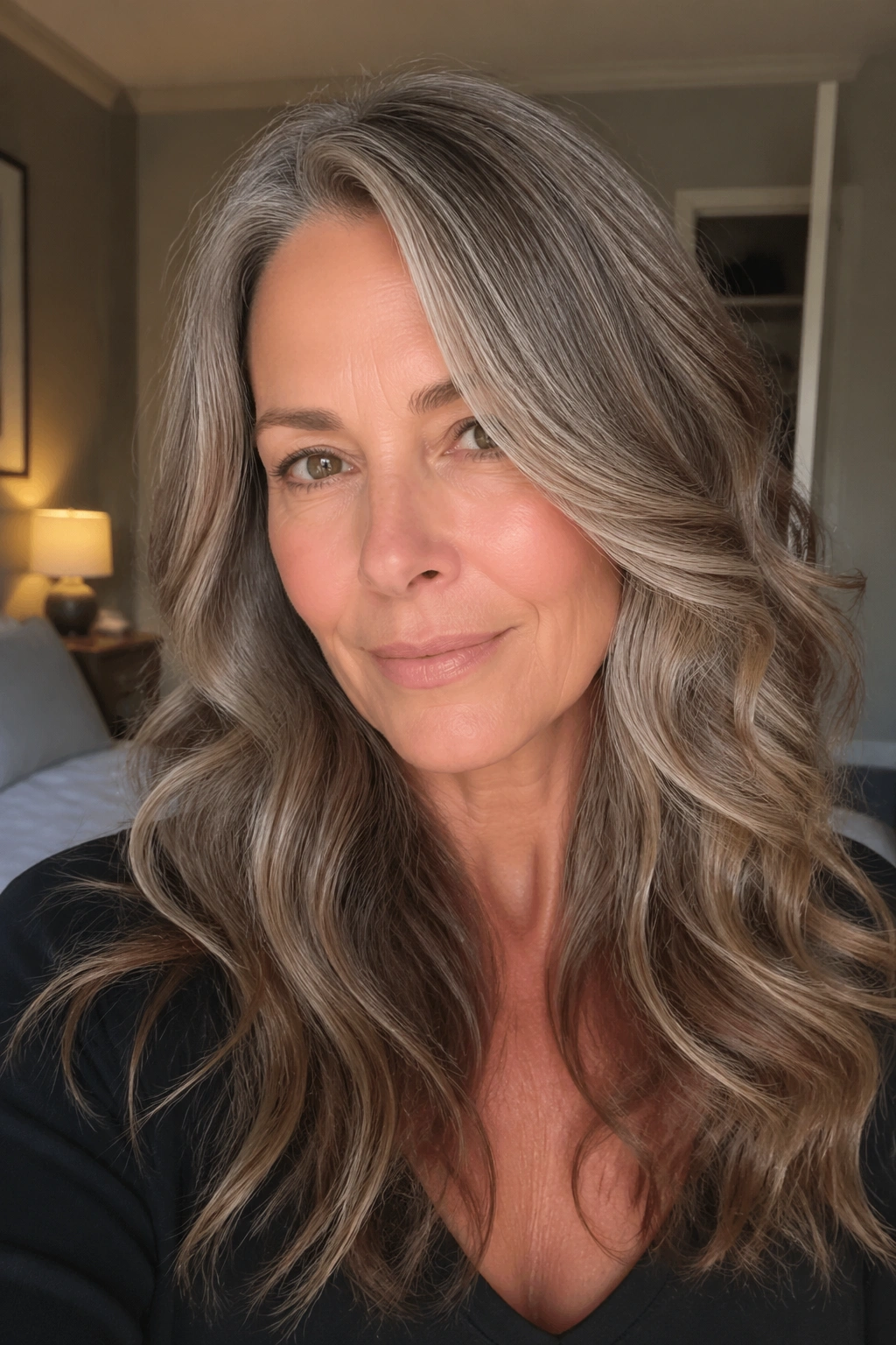 Close-up of a real woman with soft face-framing layers and a side part in warm bedroom light
