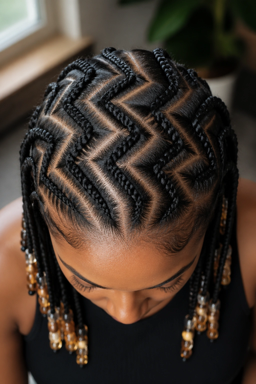 Close-up top-down view of a real person's scalp with zigzag cornrow parts and beads at the tips